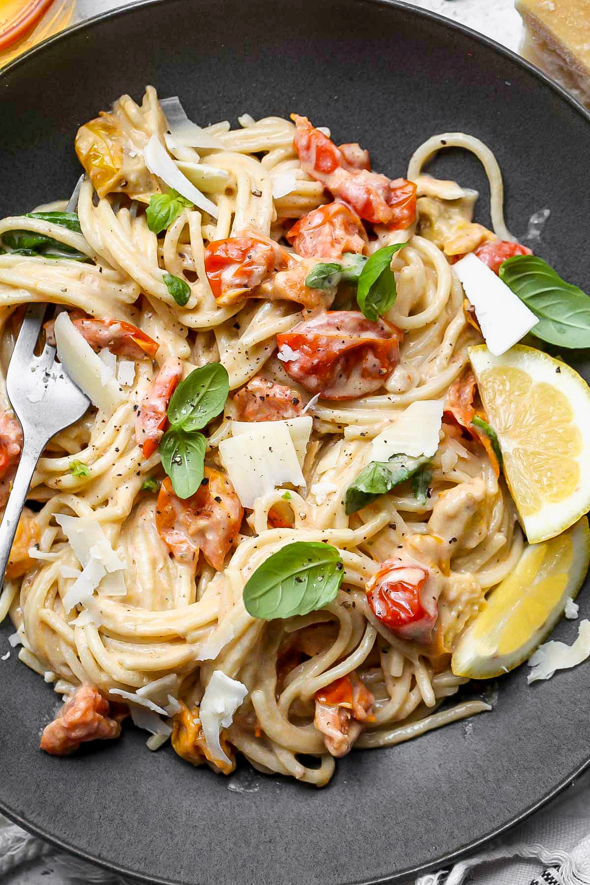 Creamy tahini pasta with burst cherry tomatoes in a grey serving bowl.