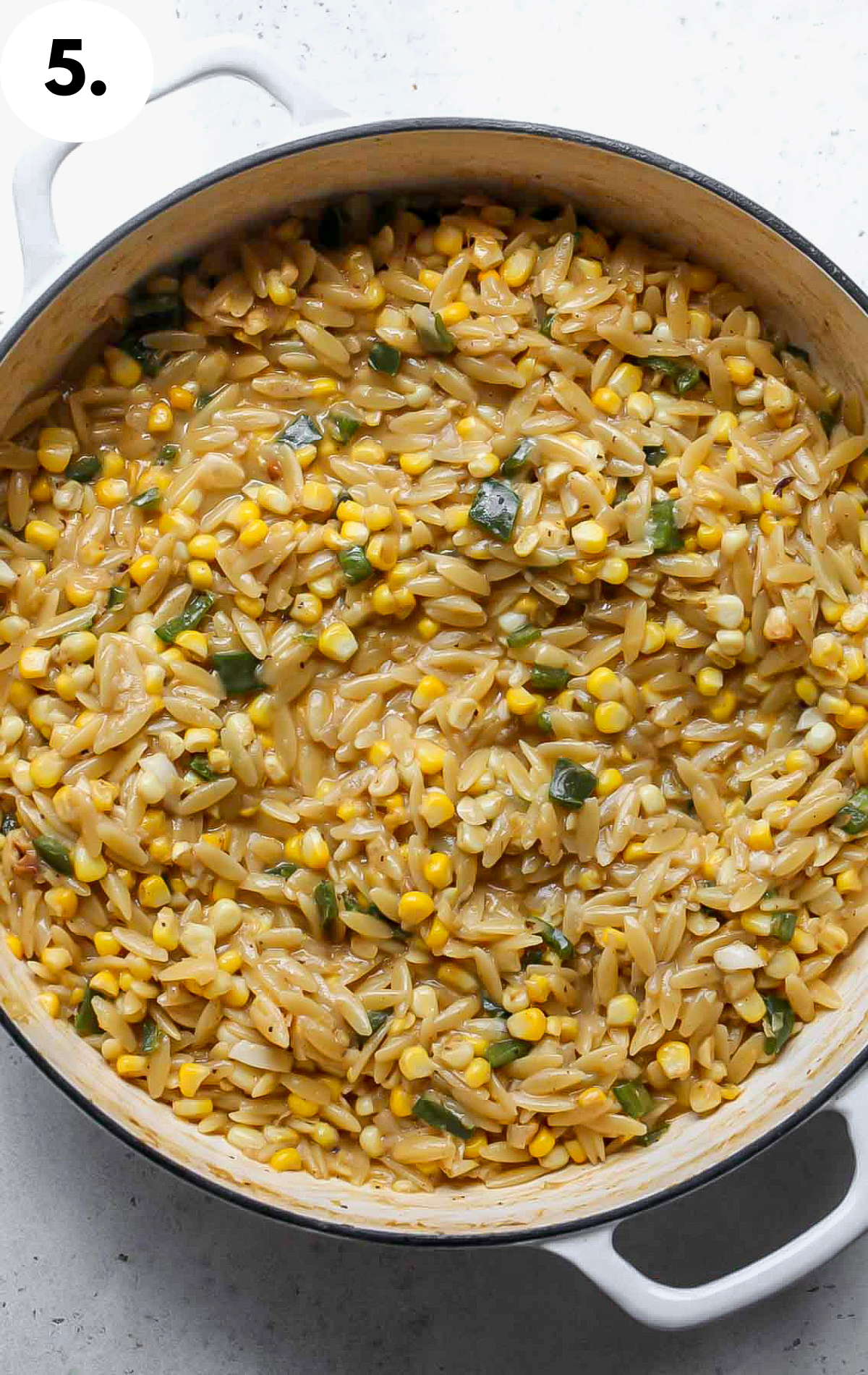 Orzo being cooked until tender in a white pan.