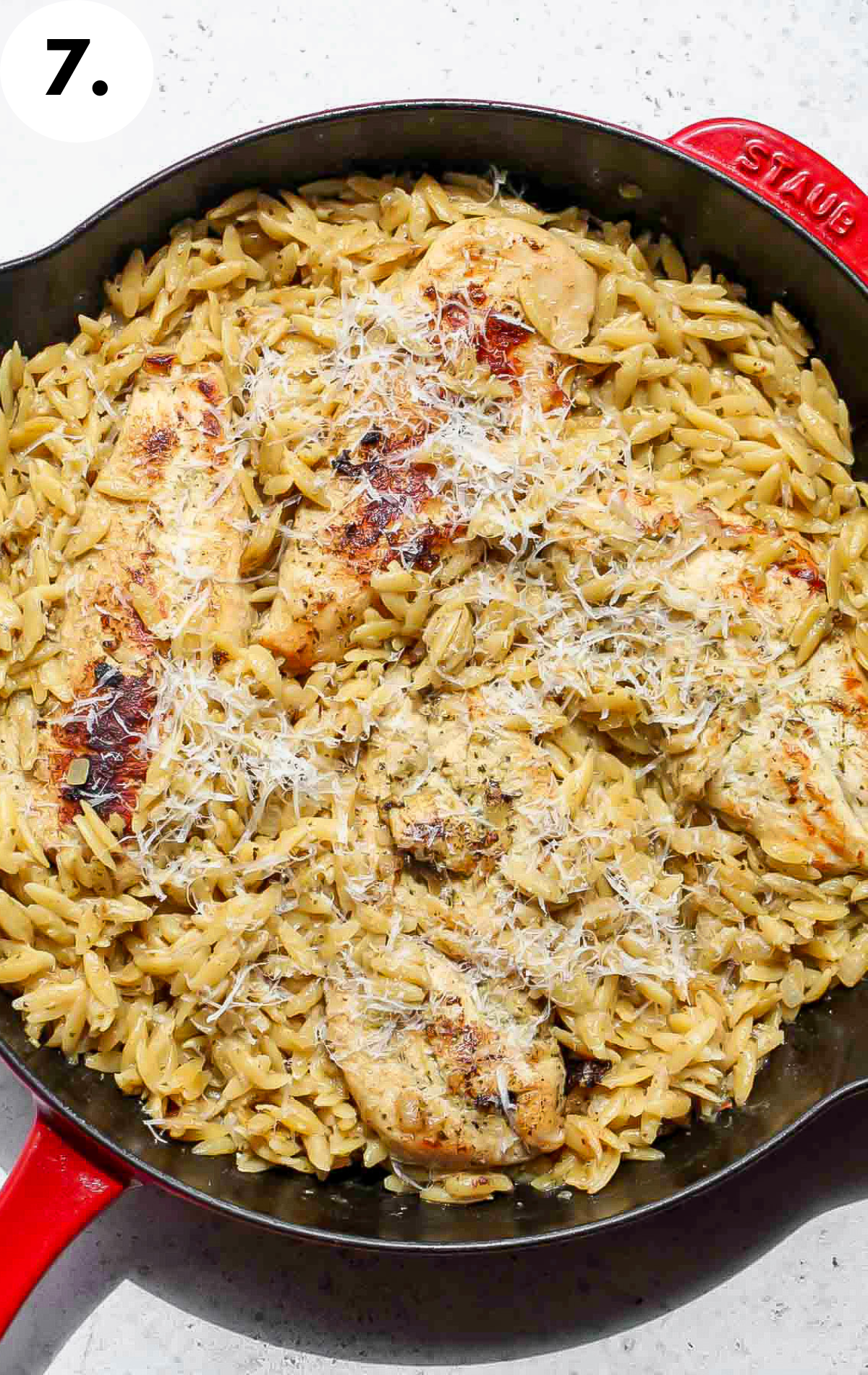 Chicken and orzo being topped with Parmesan cheese.