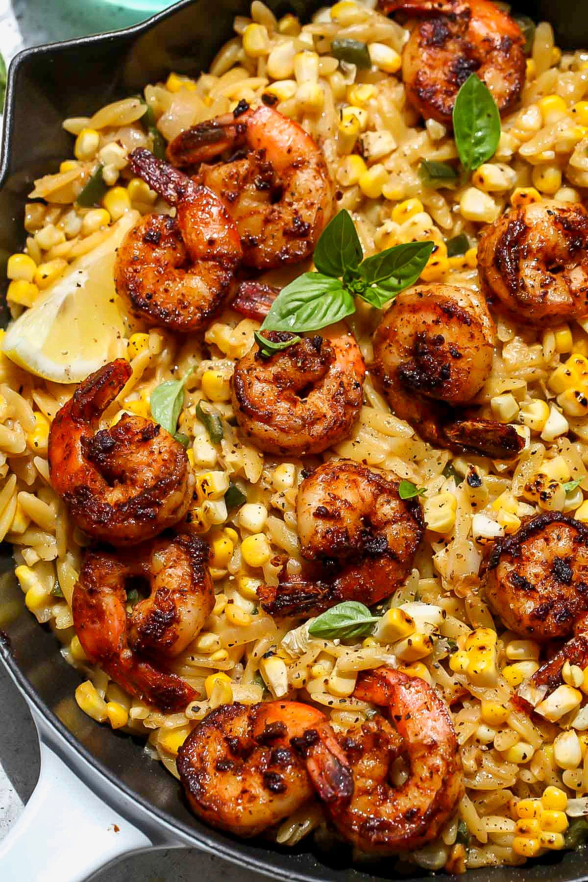 Creamed Corn Shrimp Orzo in a skillet topped with fresh basil leaves.