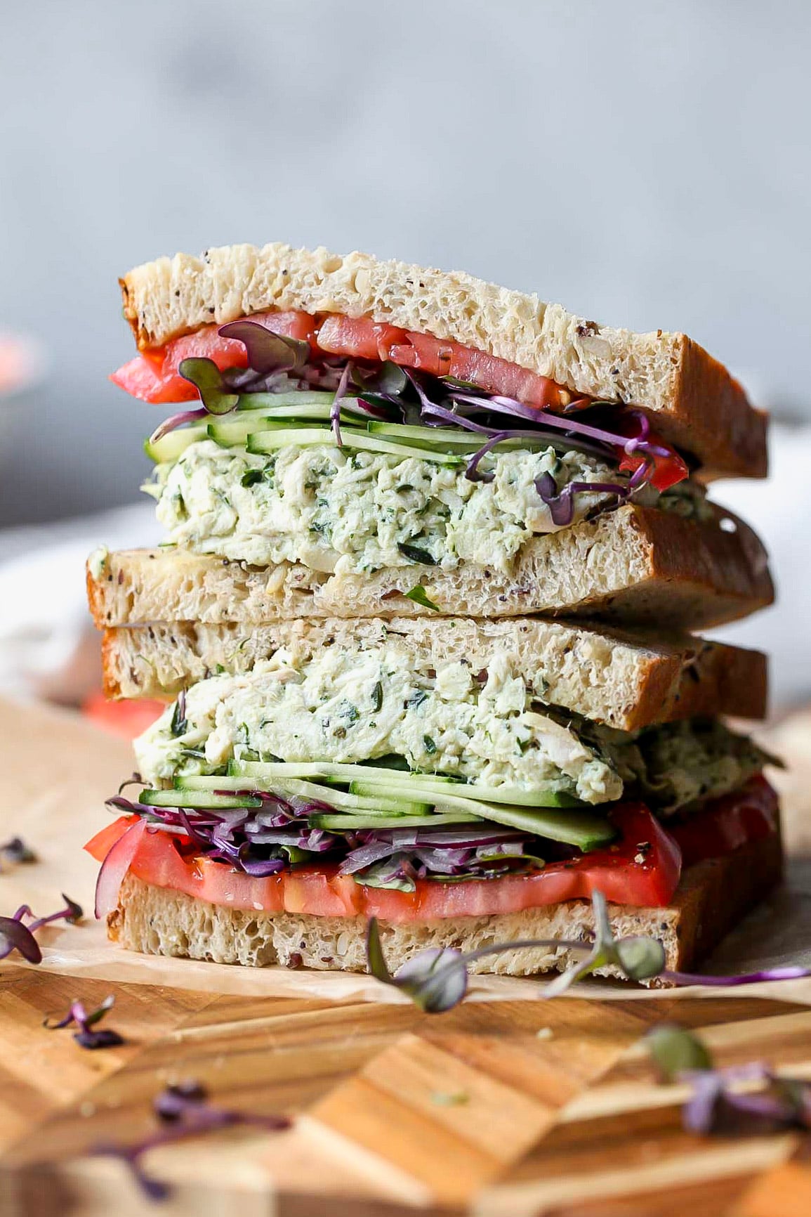 Chicken salad sandwich sliced in half and stacked on top of each other on a wooden cutting board.