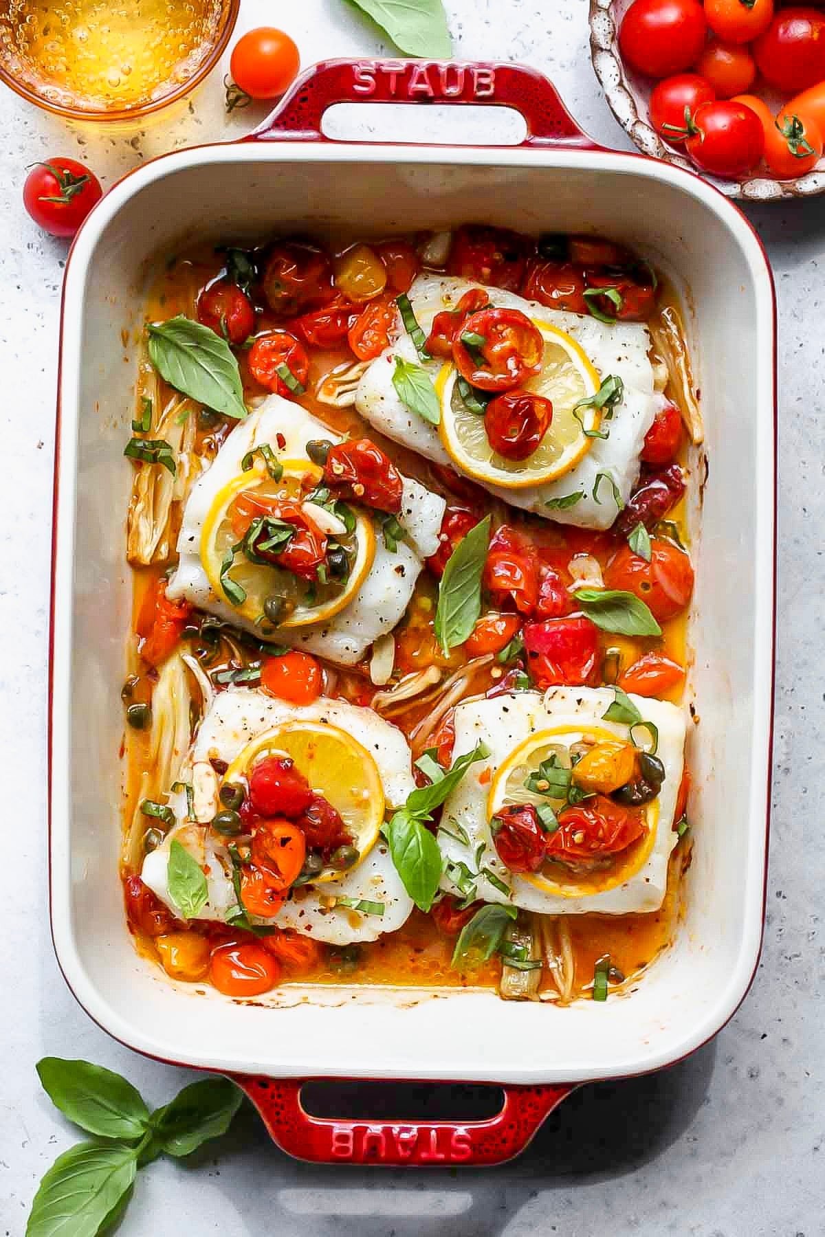 A red baking dish filled with baked Mediterranean cod.