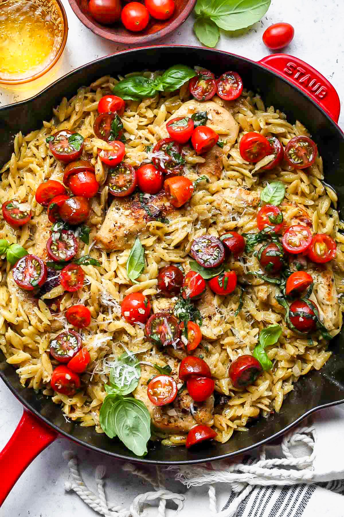 Pesto chicken and orzo in a black skillet topped with tomatoes and basil.