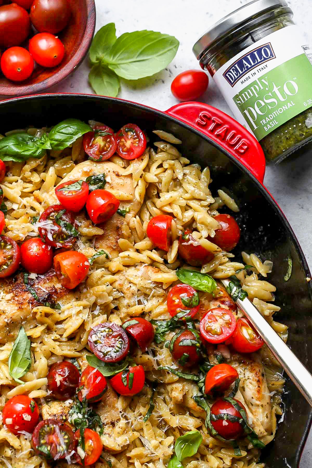 Skillet of pesto chicken and orzo next to a jar of DeLallo pesto.