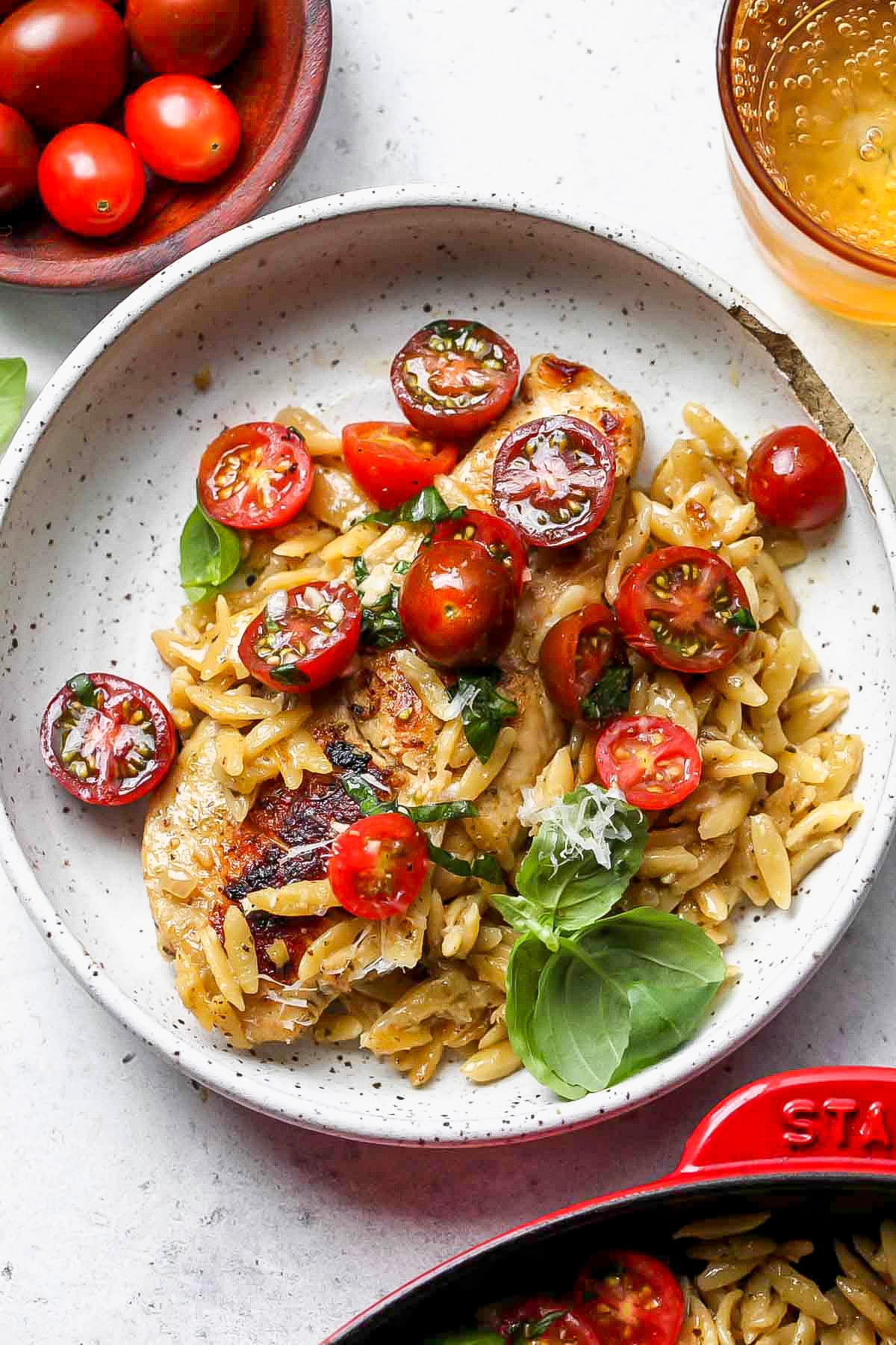 A white bowl filled with a single serving of pesto chicken, orzo, and tomatoes.