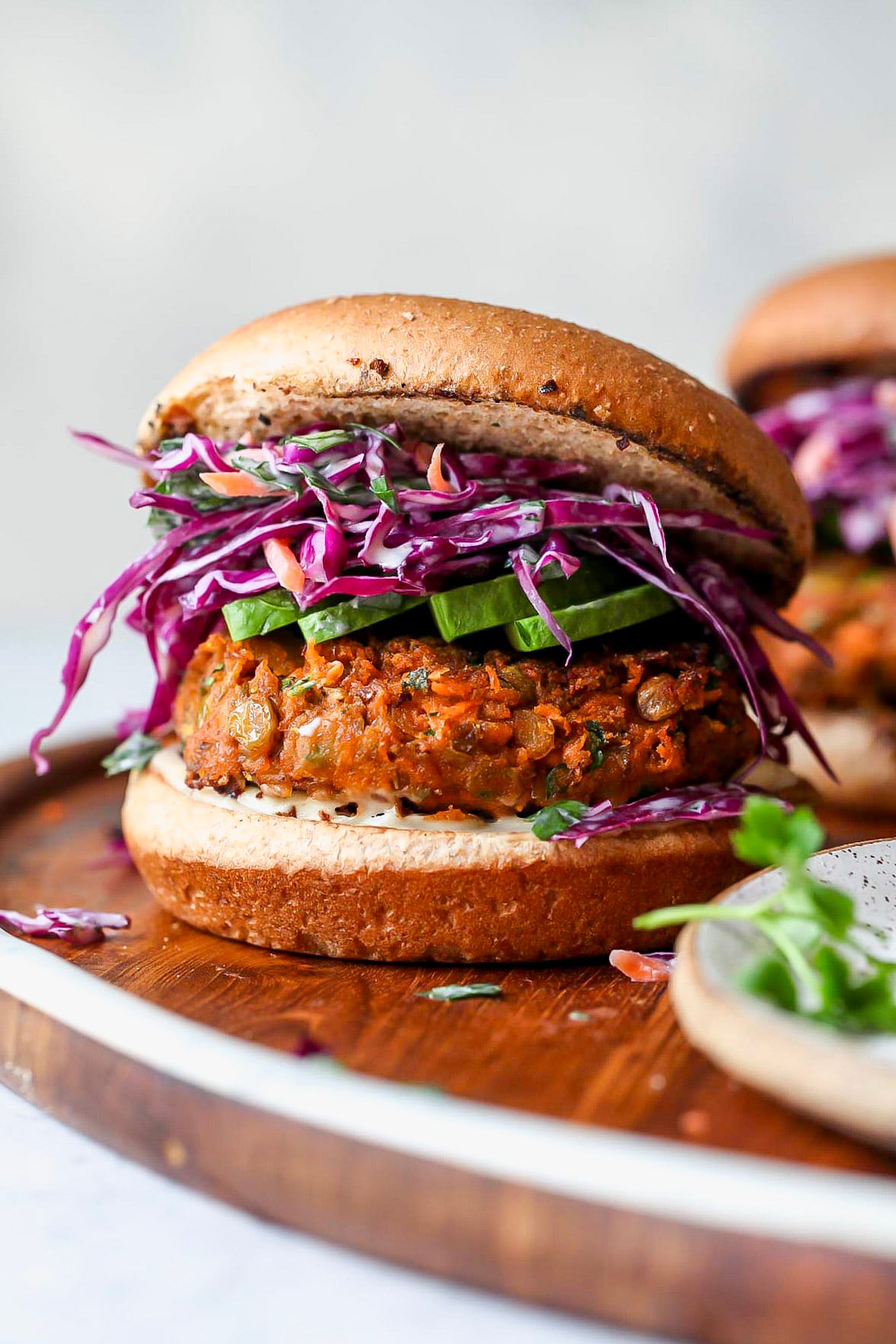 Lentil burger topped with tahini slaw on a wooden platter.