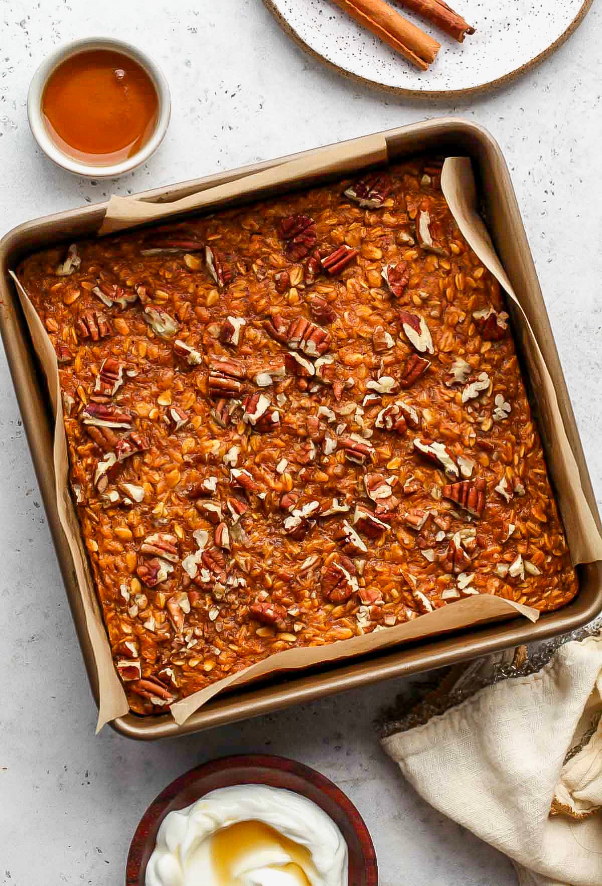 An 8x8 pan of baked pumpkin oats topped with pecans on a white countertop.