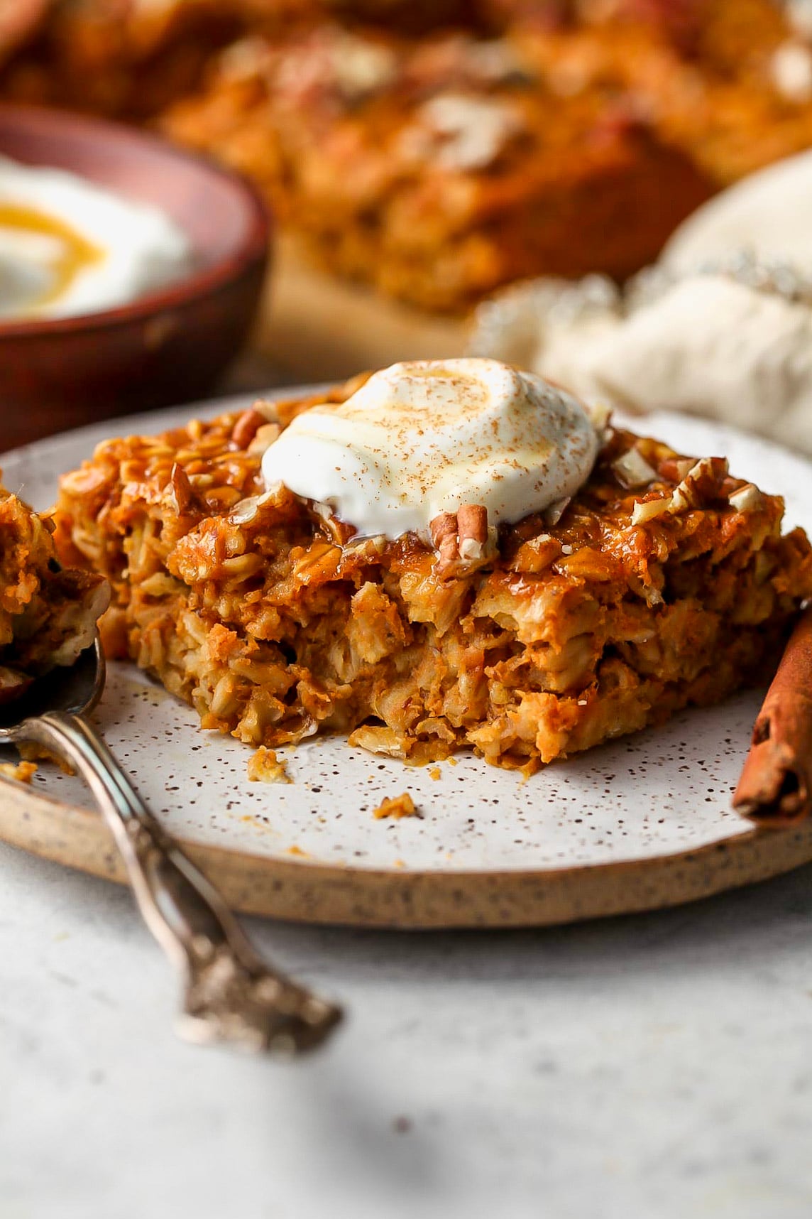 One square of baked pumpkin oats on a white plate topped with a dollop of yogurt.