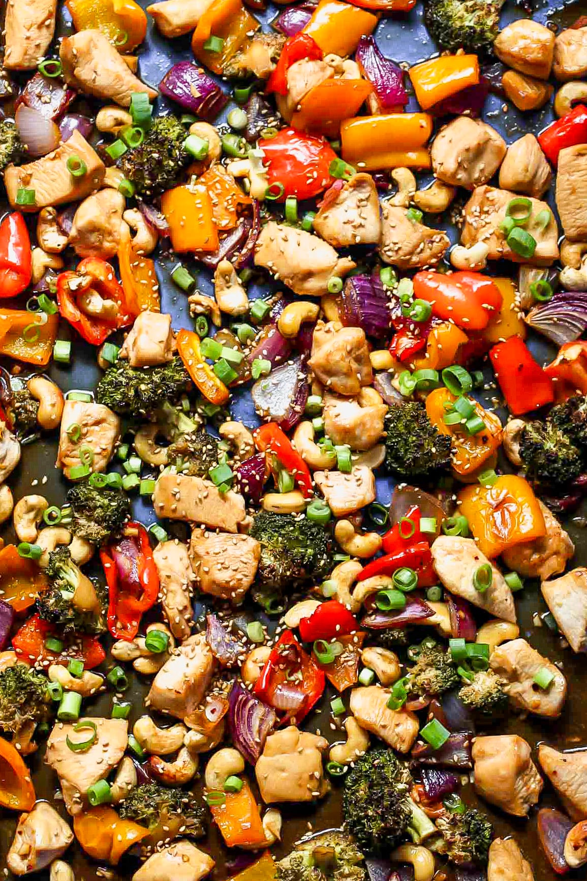 Sheet pan honey-sesame chicken and veggies mixed together on a blue baking sheet.