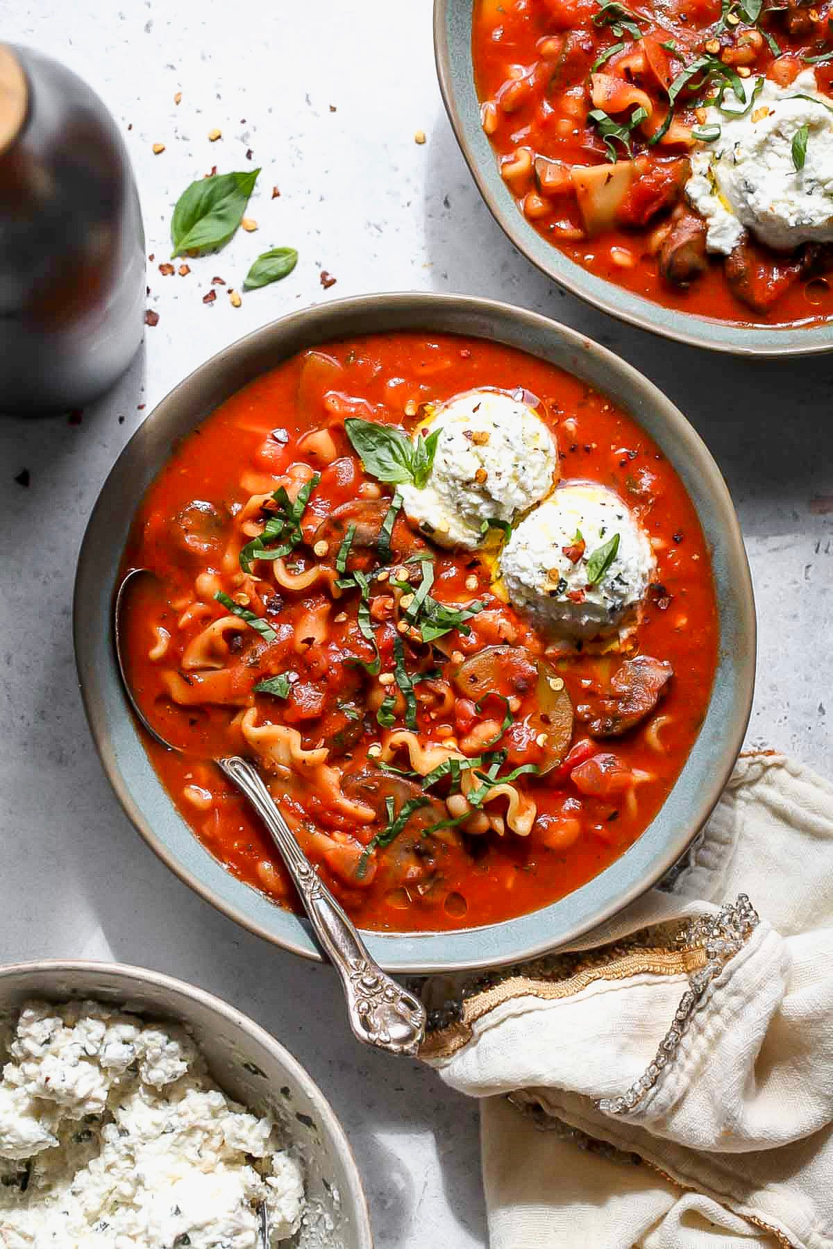 Two serving bowls filled with vegetarian lasagna soup arranged on a white surface.