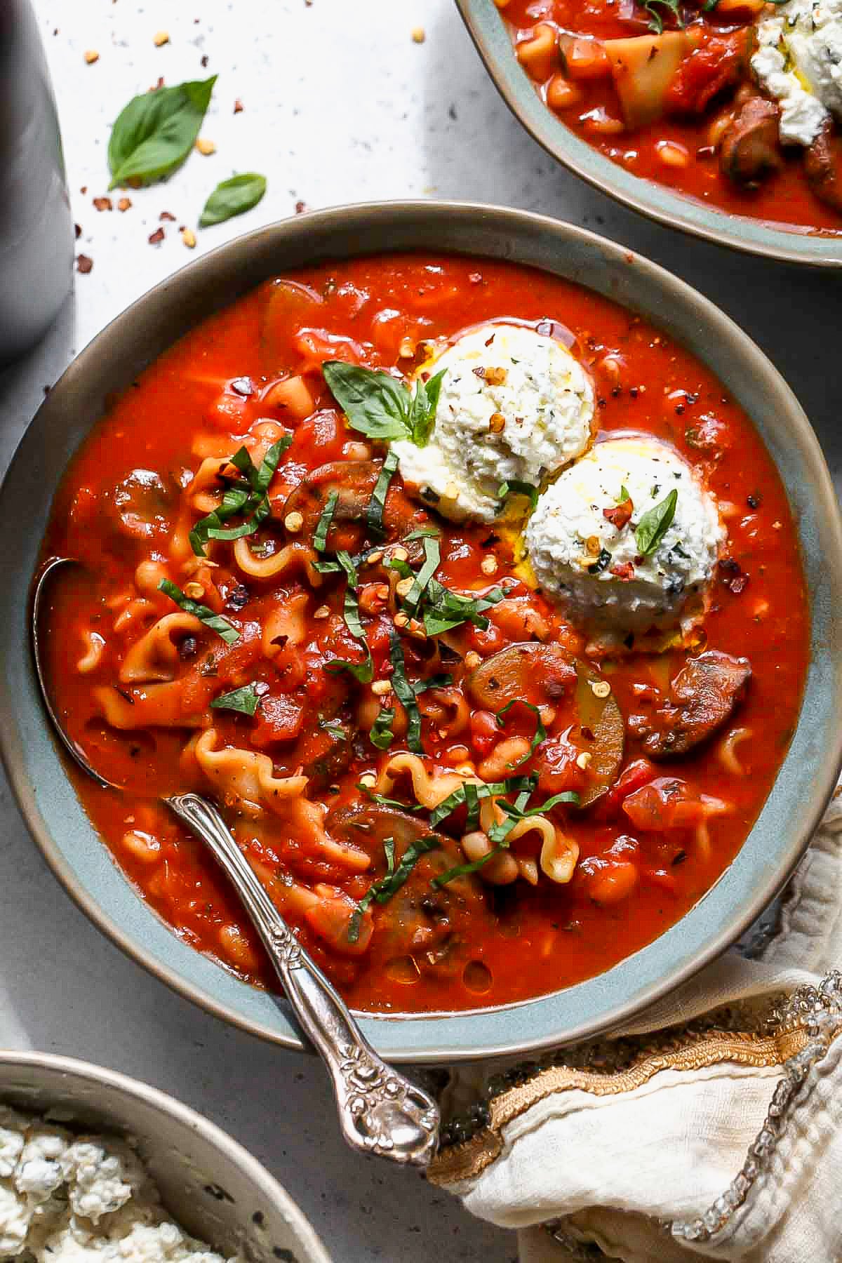 Vegetarian lasagna soup in a blue bowl topped with two dollops of herbed ricotta cheese.