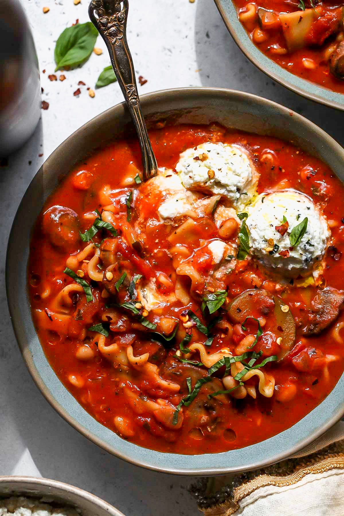 A small spoon digging into a bowl of vegetarian lasagna soup.