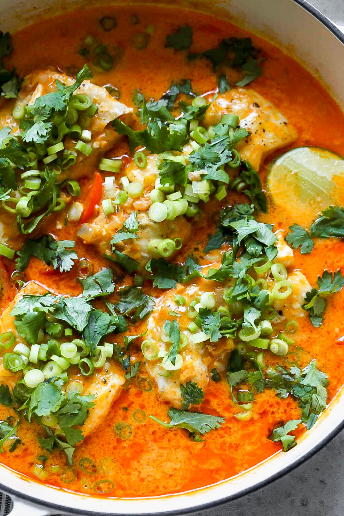 Thai coconut cod in curry sauce arranged in a white pan topped with cilantro and green onion.