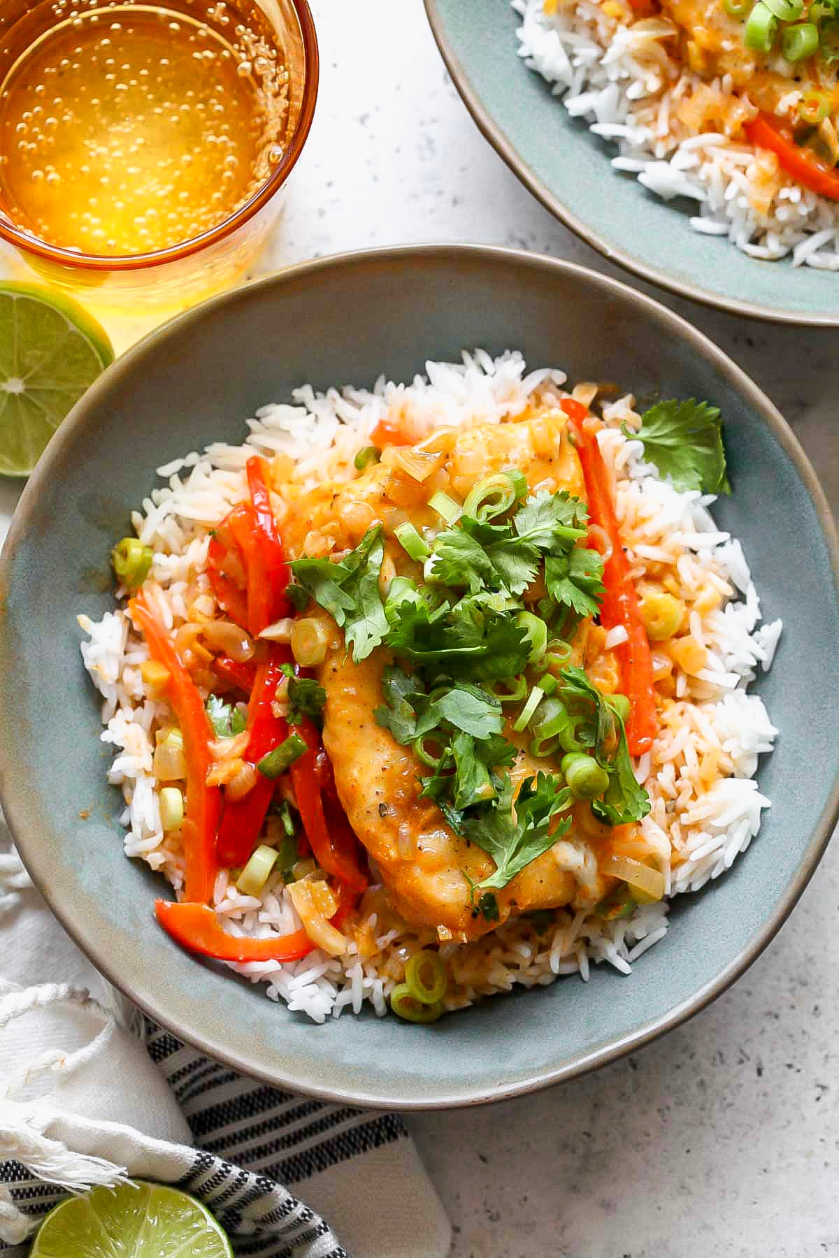 One fillet of cod over a bed of rice in a blue bowl topped with coconut curry sauce and herbs.