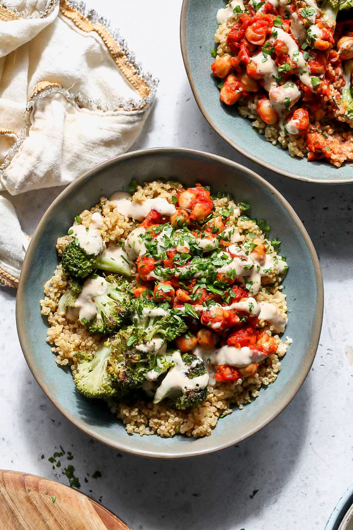 Chickpea and broccoli bowls drizzled with garlic sauce styled in two light blue bowls.