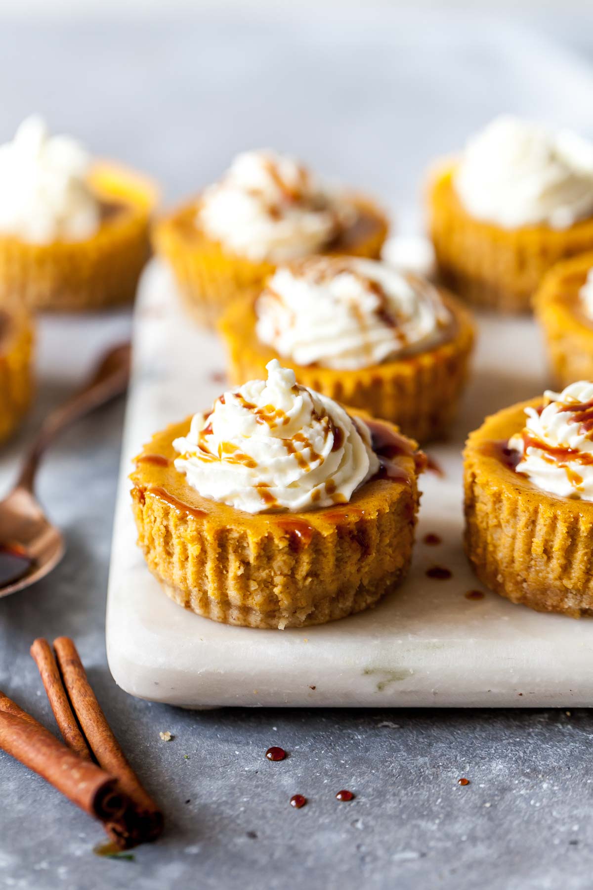 Mini pumpkin cheesecakes topped with whip topping arranged on a white serving platter.