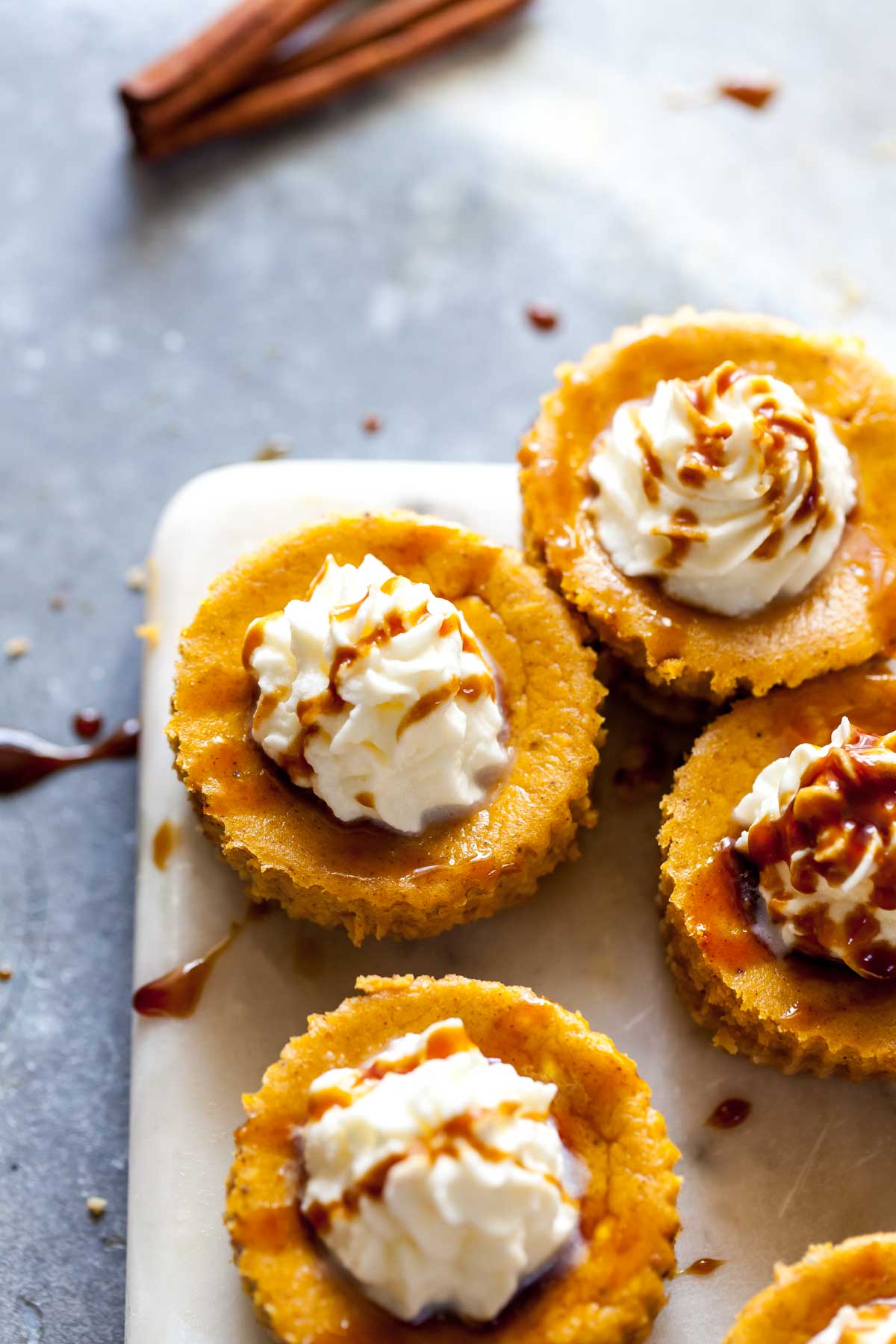 Mini pumpkin cheesecakes with whipped topping arranged on a white serving platter.