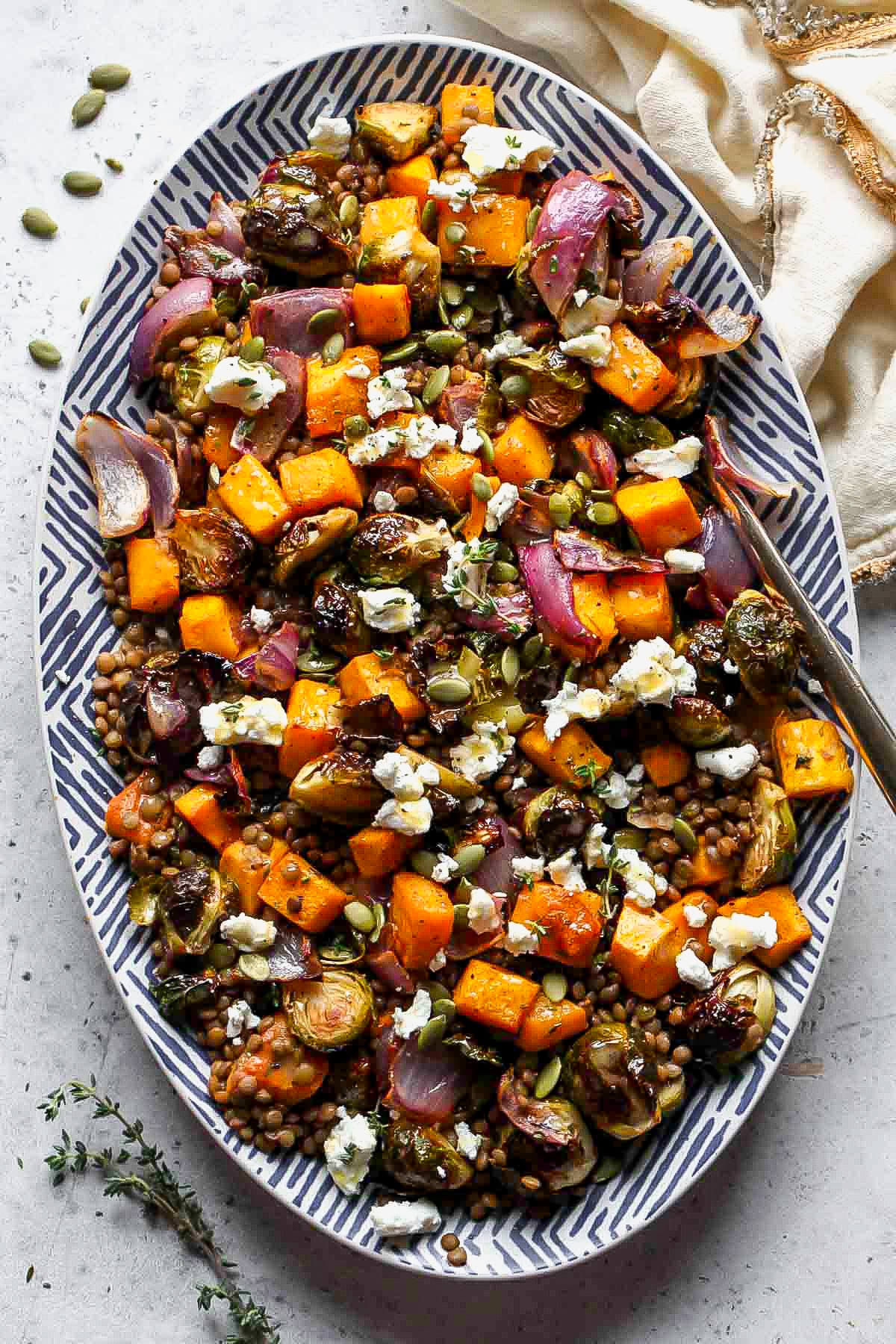 Roasted veggie lentil salad arranged on an oval blue-stripped serving platter.