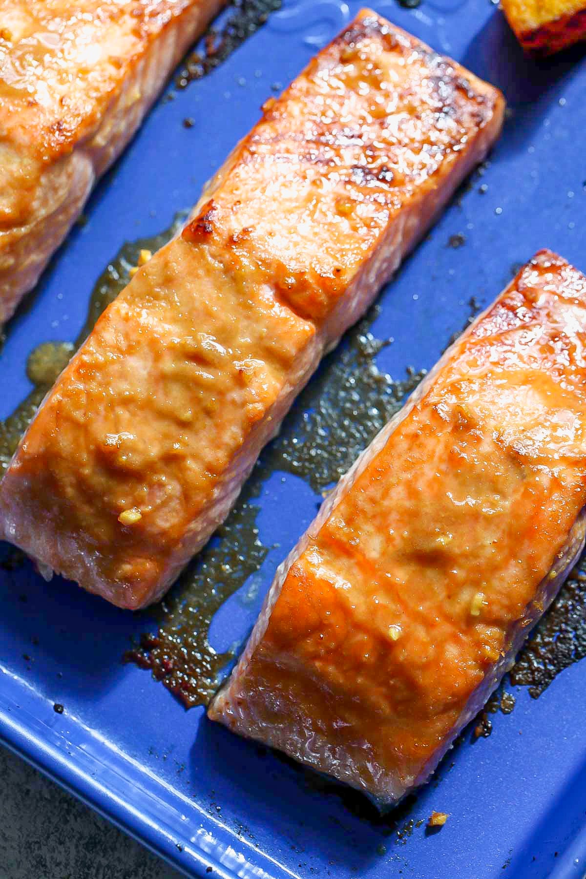 Salmon fillets topped with a miso-ginger glaze on a blue baking sheet.