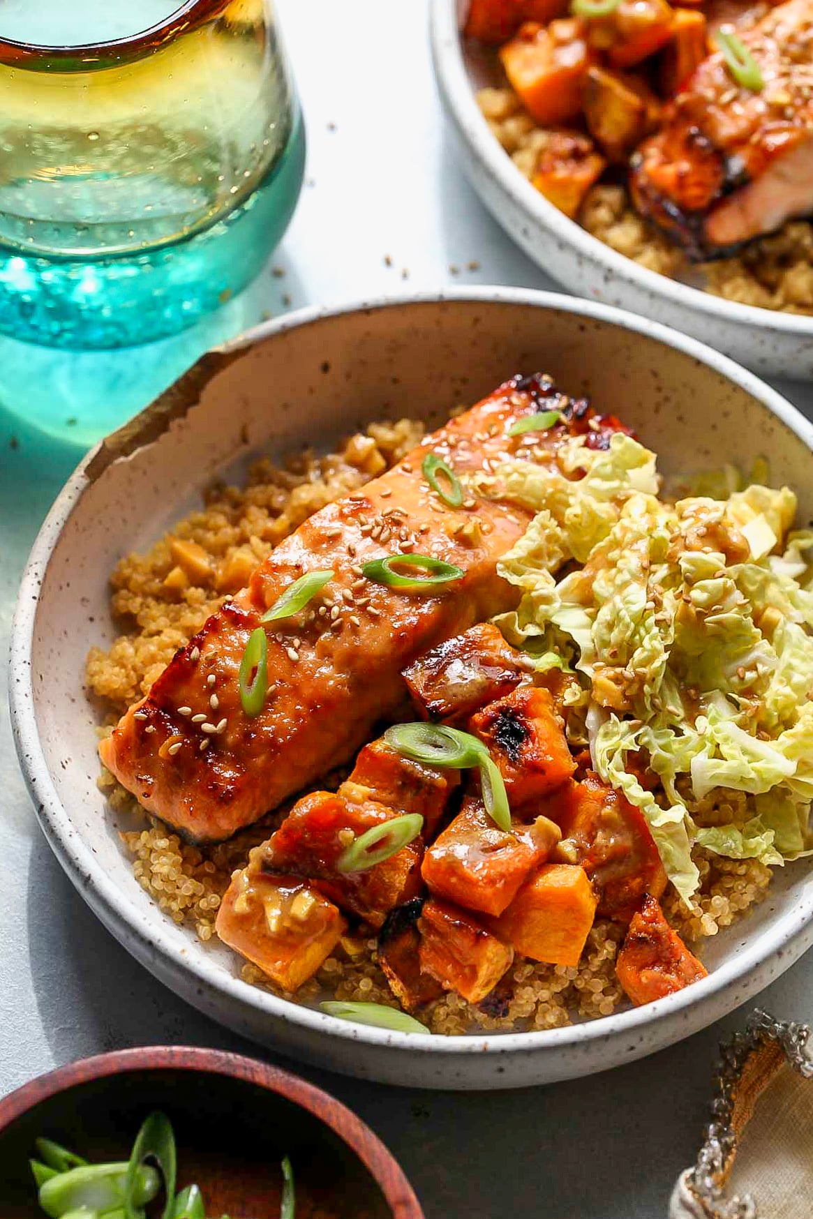 Miso-ginger salmon, squash, and cabbage styled over a bed of quinoa in a white speckled bowl.