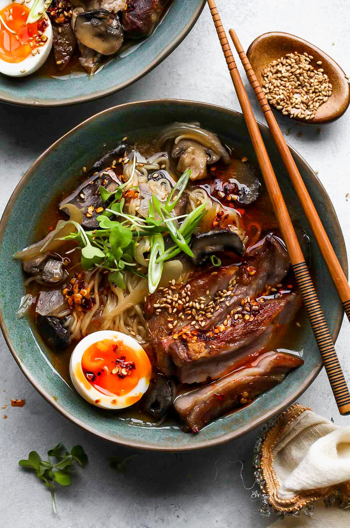 Slow cooker pork ramen assembled in a blue bowl topped with a soft-boiled egg and green onion.