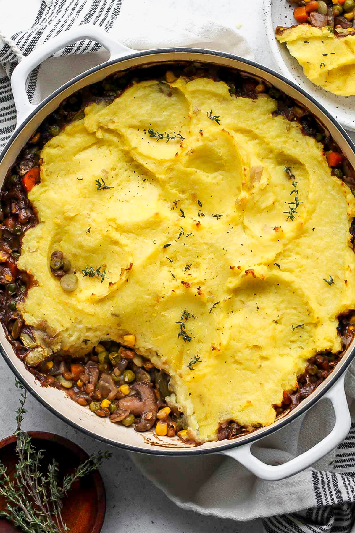 Vegetarian shepherds pie in a round white pan with a scoop missing to show the inside filling.