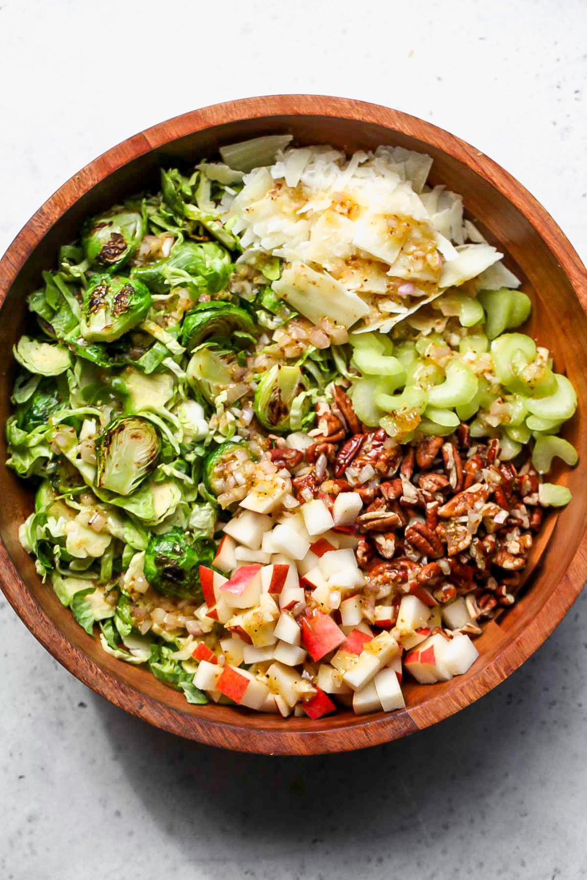 A large wooden bowl filled with sprouts, pecans, celery, cheese, and pear, with mustard dressing being poured overtop.