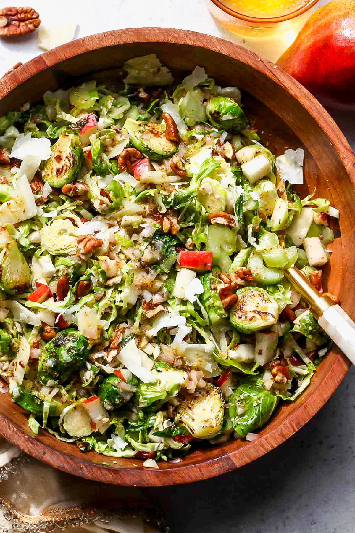 Two gold salad spoons tossing a Brussels salad. Bowl styled on a grey surface.