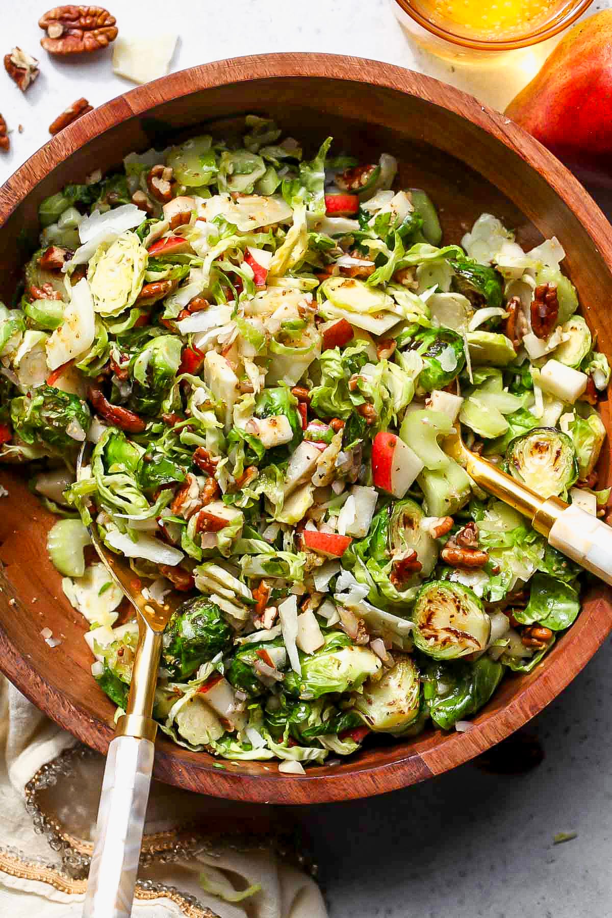 Brussels Salad being tossed in a wooden bowl with two gold salad spoons.