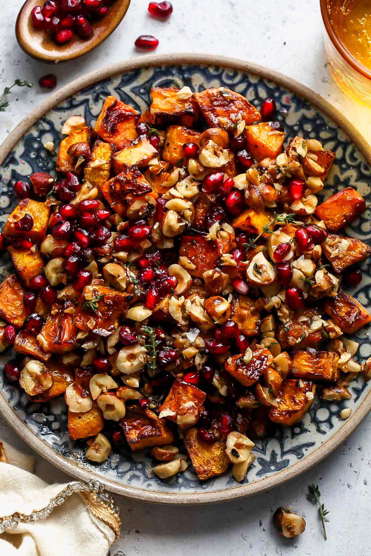 Roasted butternut squash topped with brown butter hazelnuts and pomegranate on a blue and white plate.