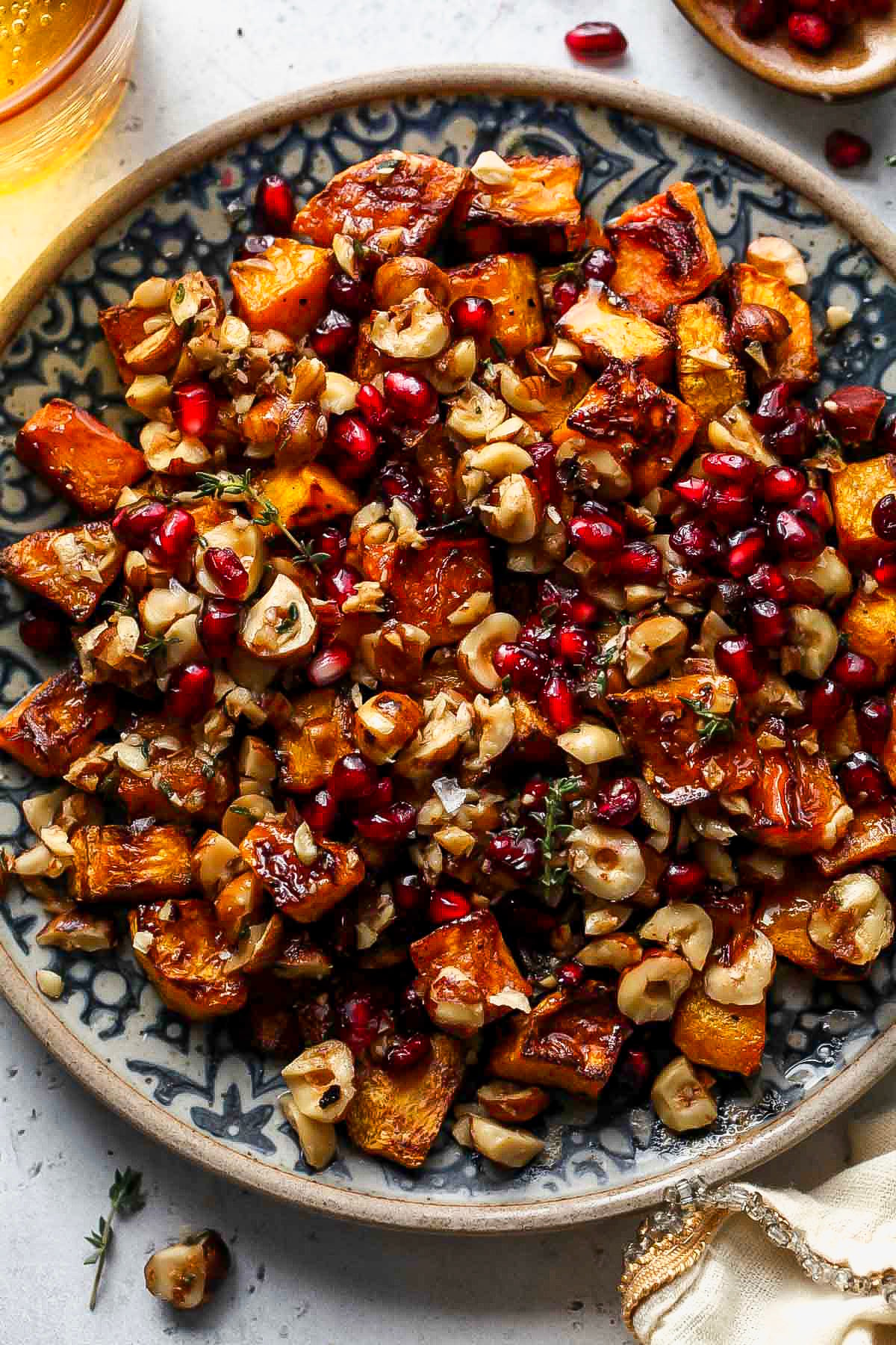 A blue and white patterned plate with roasted butternut squash cubes, brown butter hazelnuts, and pomegranate seeds.
