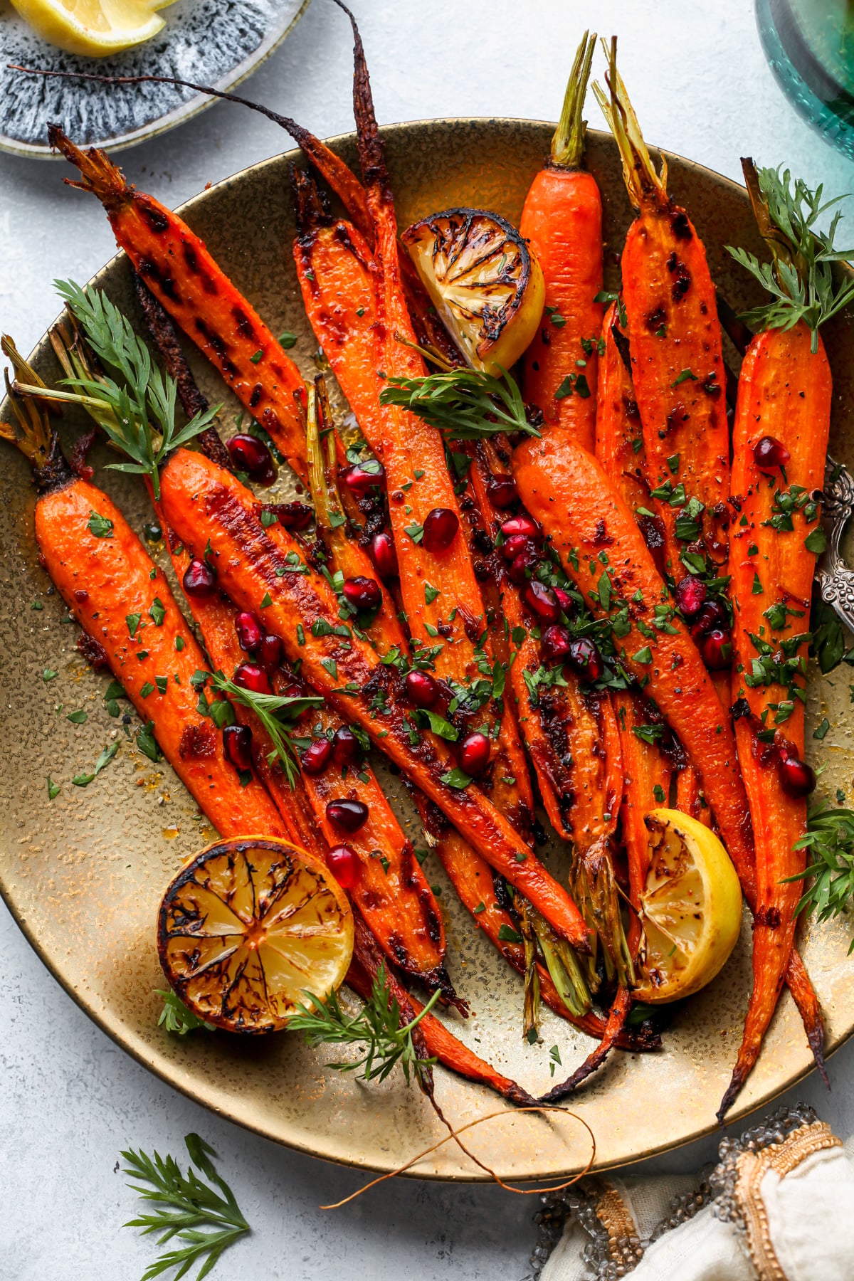 Honey-Harissa roasted carrots arranged on a gold plate topped with parsley and pomegranate.