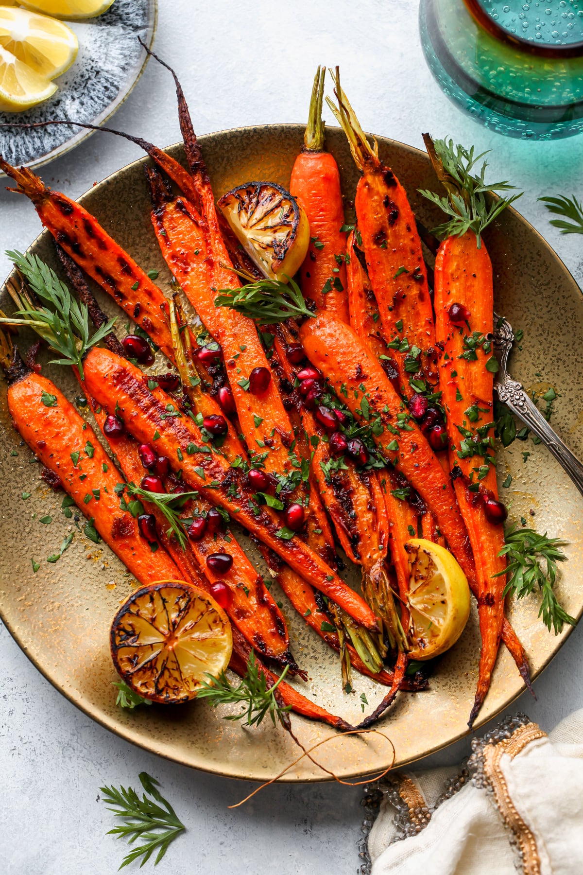 Harissa-honey roasted carrots arranged on a gold serving platter on a grey surface.