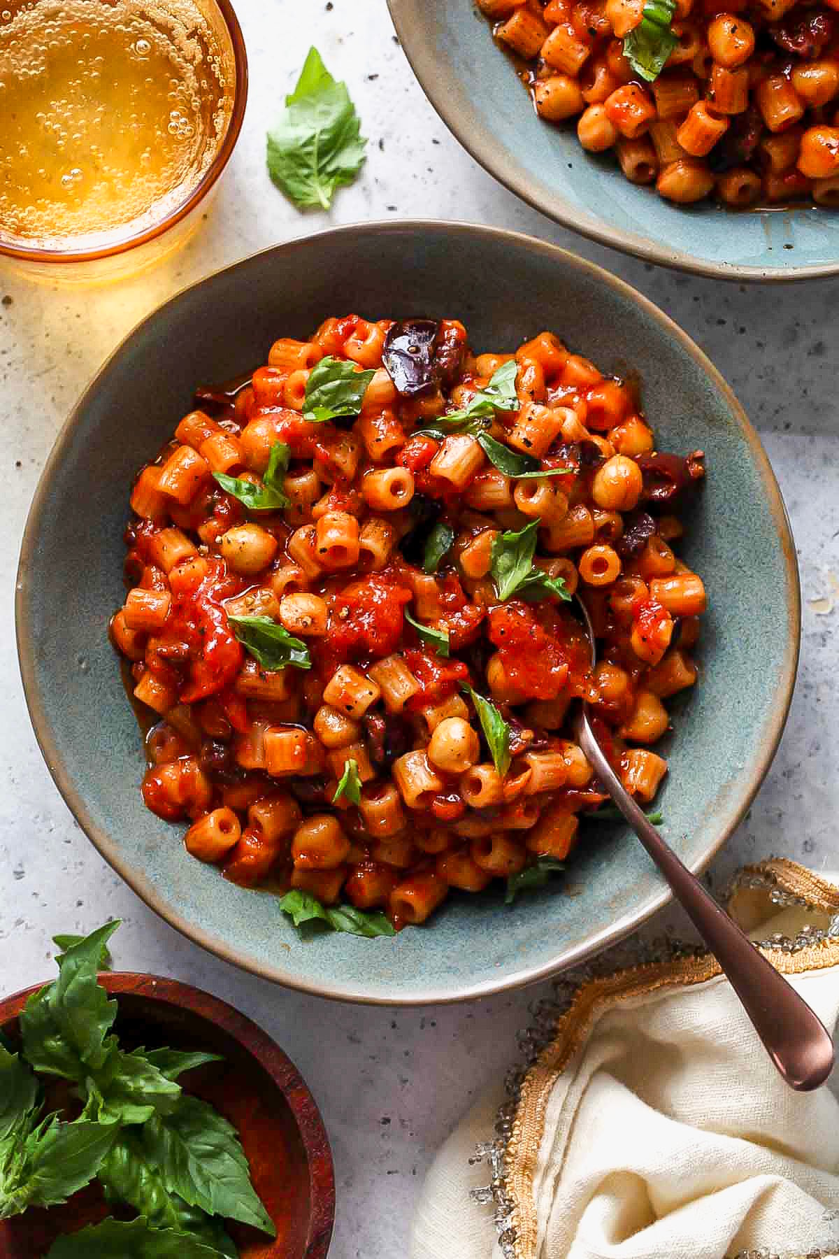 One pot puttanesca with chickpeas in a blue bowl with a spoon resting on the right side.