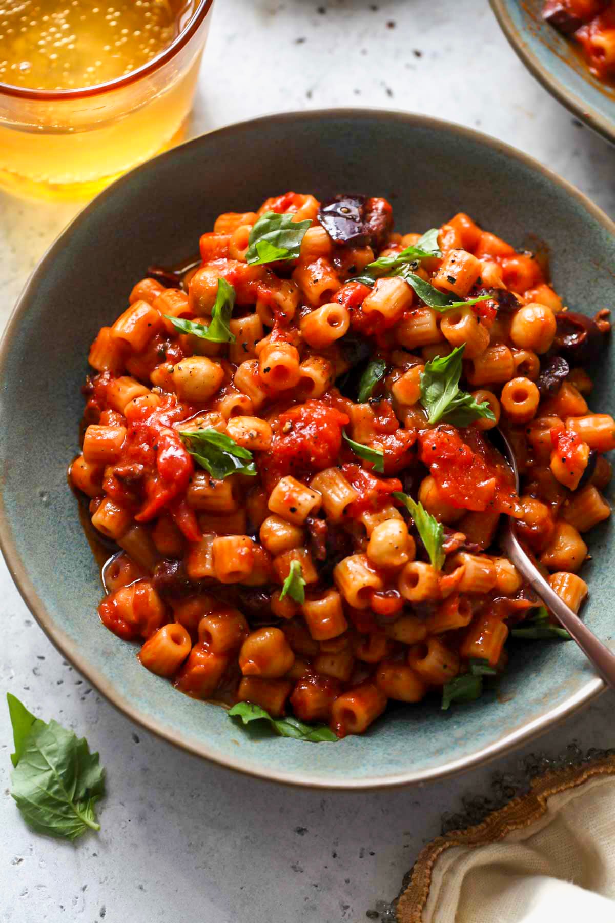 A blue bowl filled with Puttanesca with chickpeas and torn basil leaves.