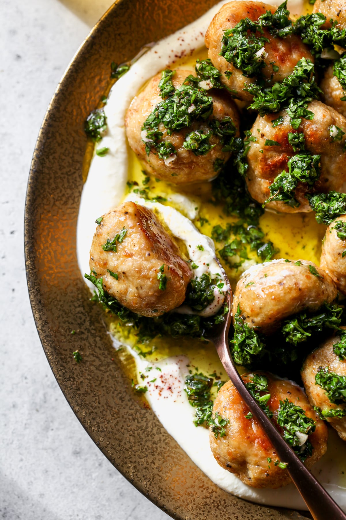 A spoon scooping up a chicken meatball on a gold serving platter.