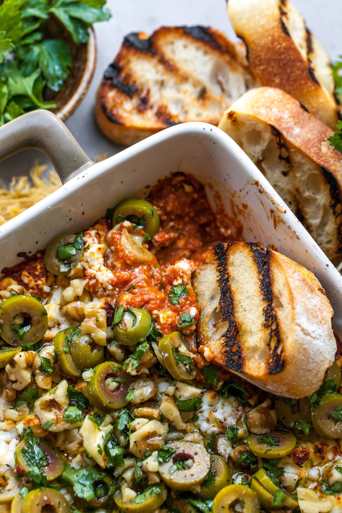 A piece of grilled bread being dipped into a dish of Moroccan baked feta.