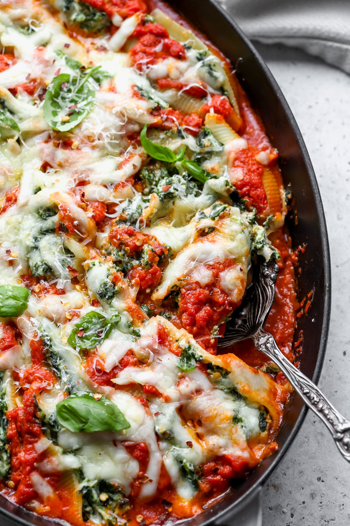 A serving spoon digging into a pan of pesto stuffed shells.