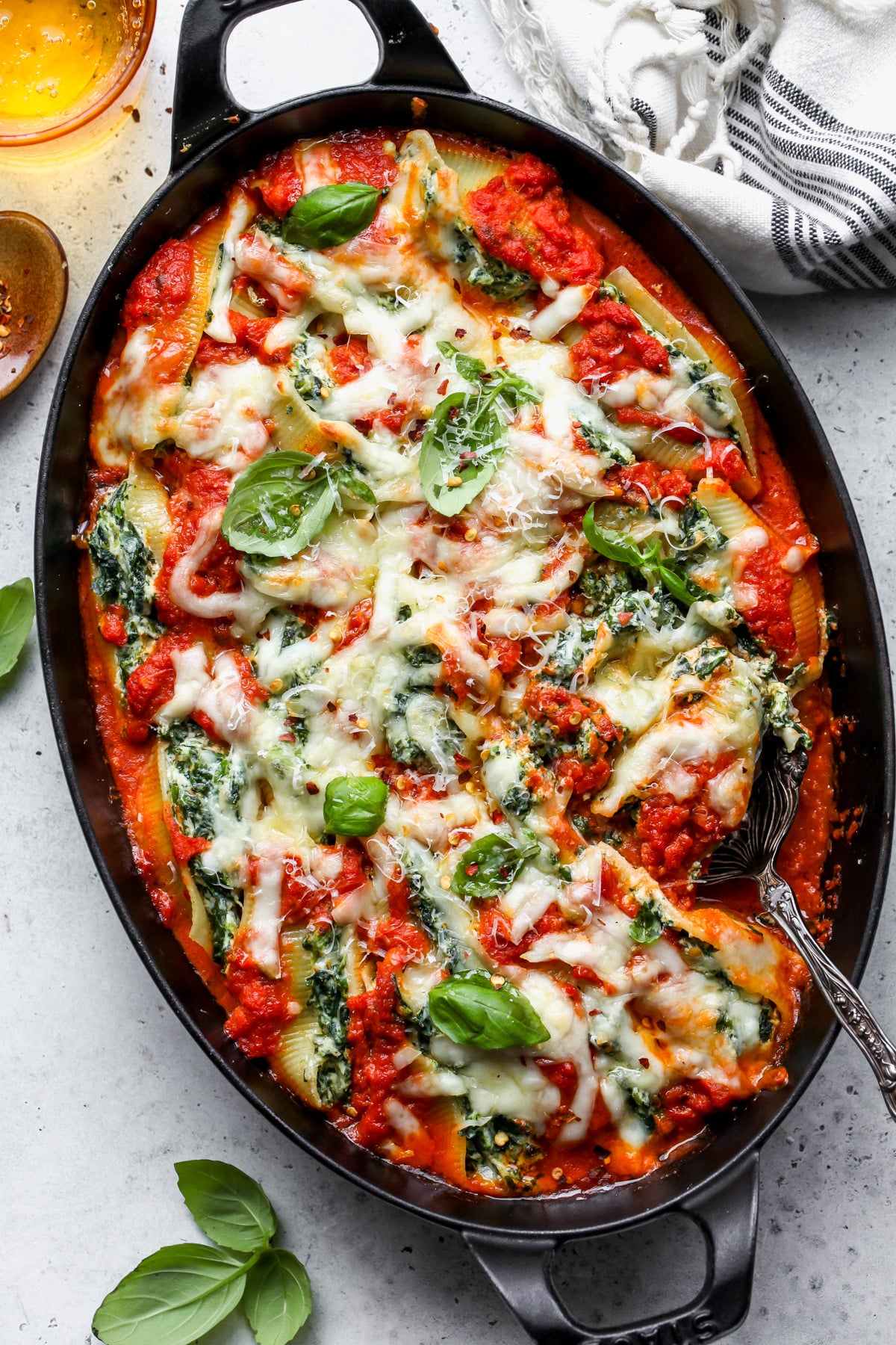 Pesto stuffed shells in vodka sauce arranged in a casserole dish topped with fresh basil leaves.