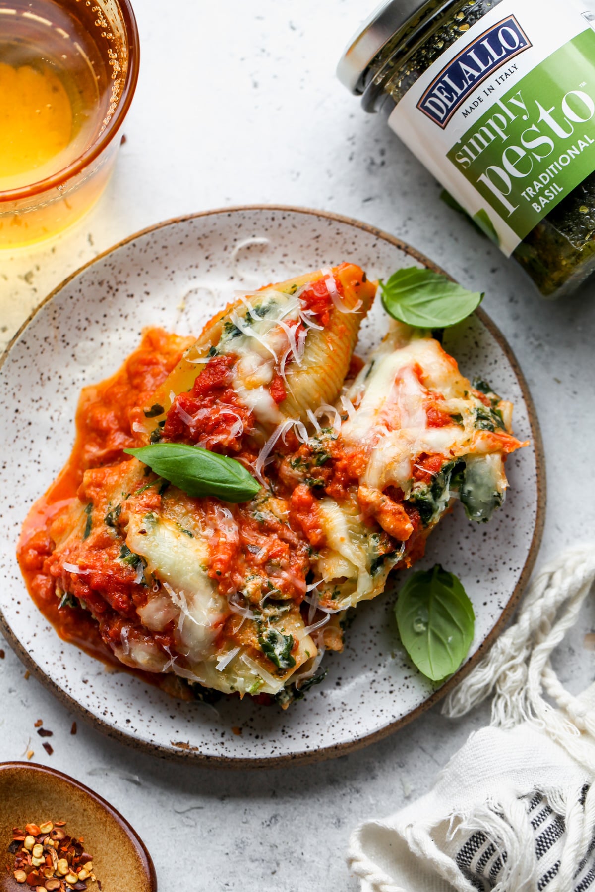 A single portion of stuffed shells on a small white plate arranged next to a jar of pesto sauce.