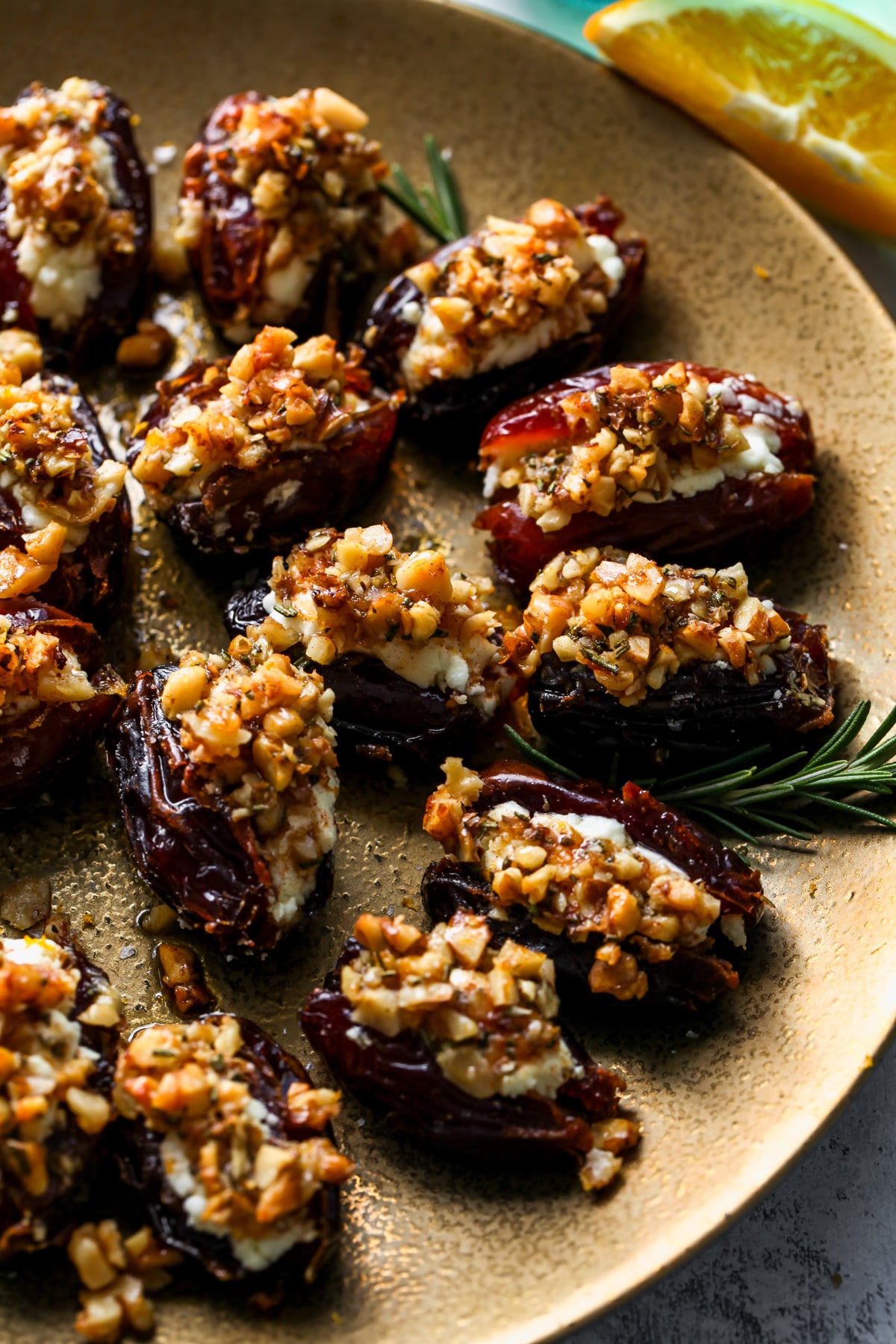 Goat cheese stuffed dates arranged on a gold plate with sprigs of rosemary.