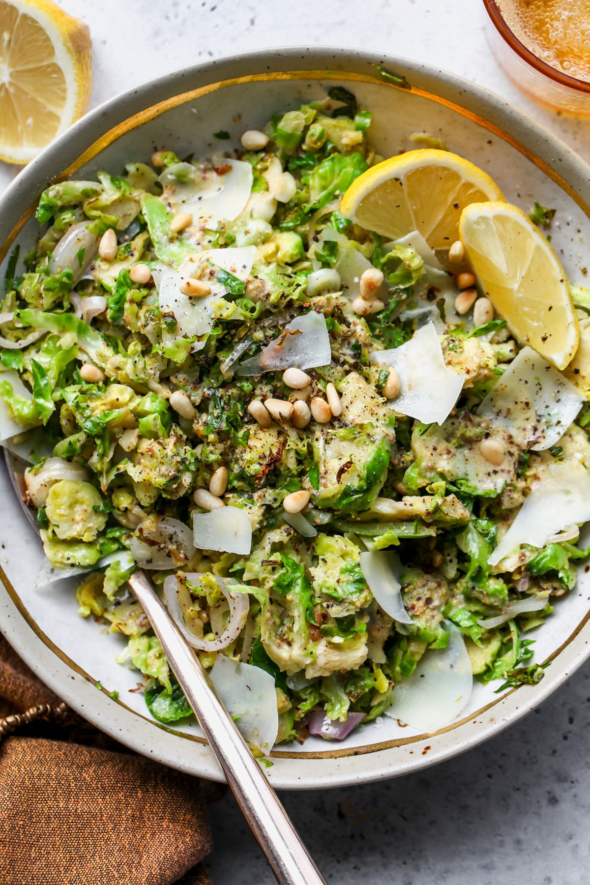 Warm Brussels salad tossed in mustard dressing in a white and gold bowl with a serving spoon on the left side.