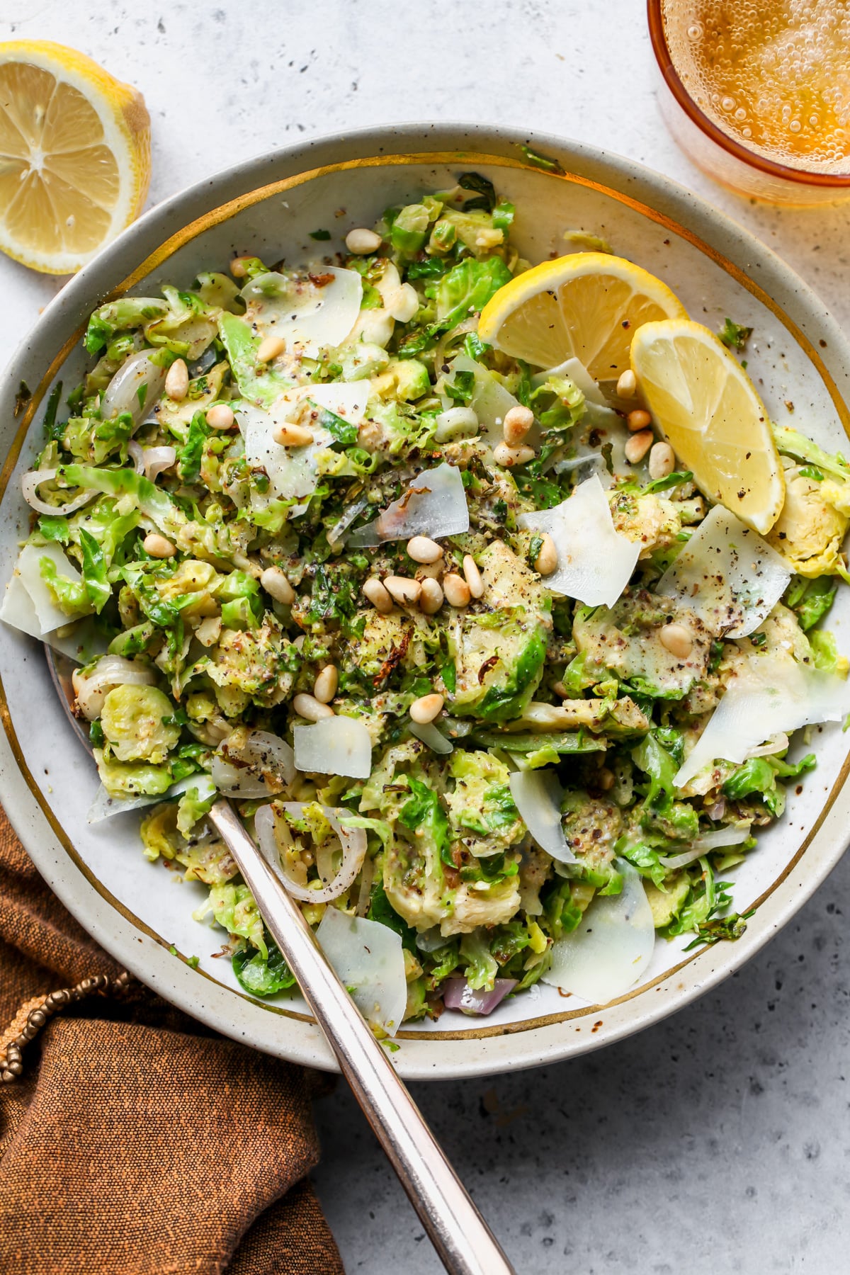 Shredded Brussels Salad styled in a tan and gold bowl with lemon wedges on the right side.