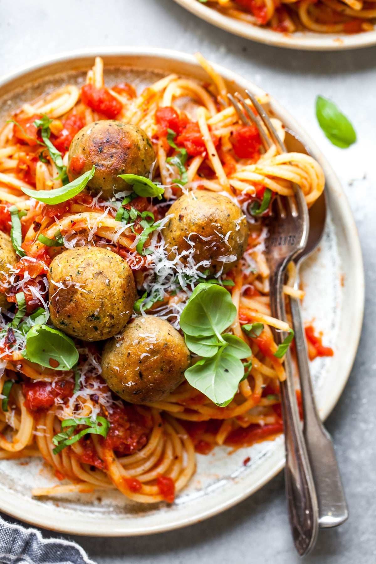 Chickpea meatballs styled over a plate of spaghetti. Fork twirling the noodles resting on the right side.