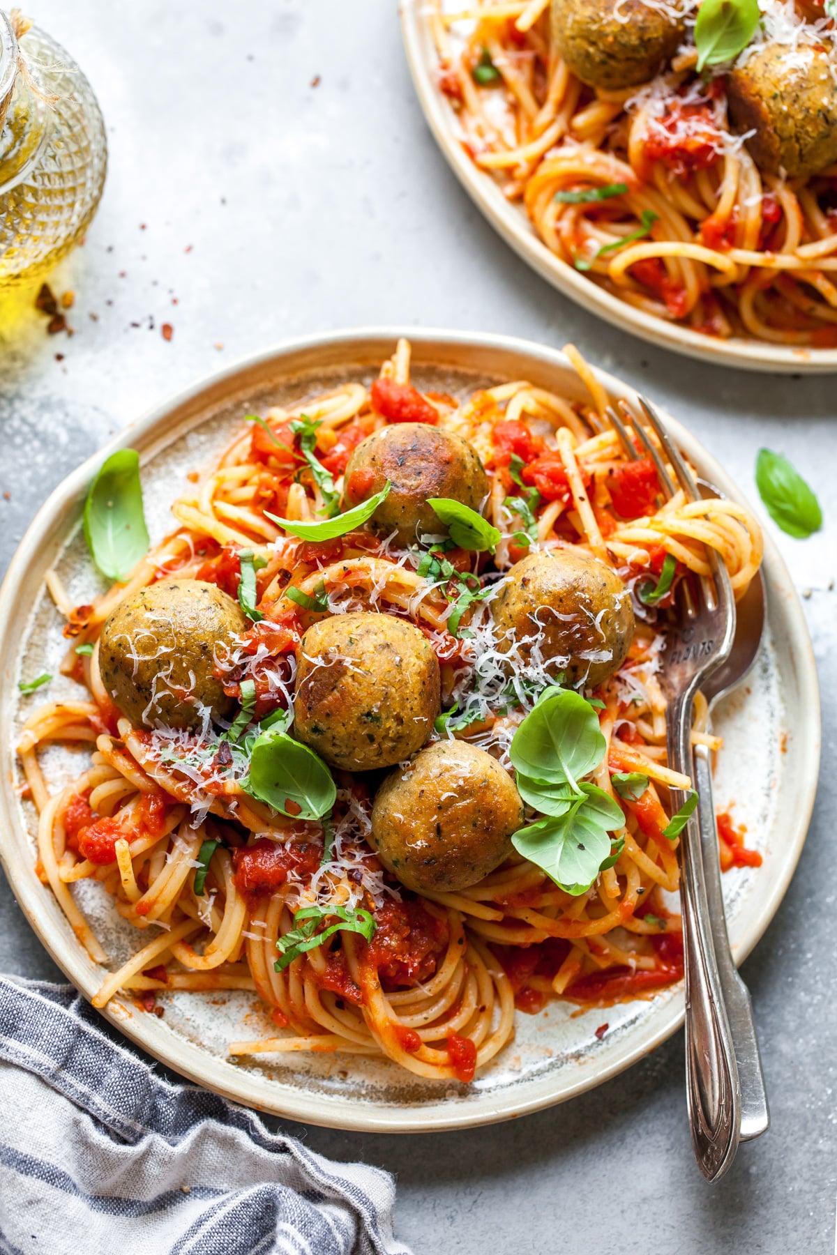 Chickpea meatballs over a plate of spaghetti in red sauce. Styled on a grey surface.