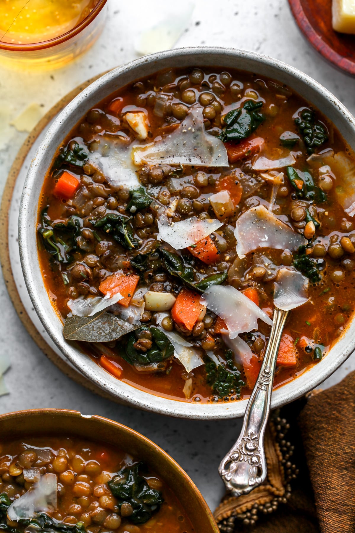 A small white soup bowl filled with lentil soup and Parmesan. Styled on a grey surface.
