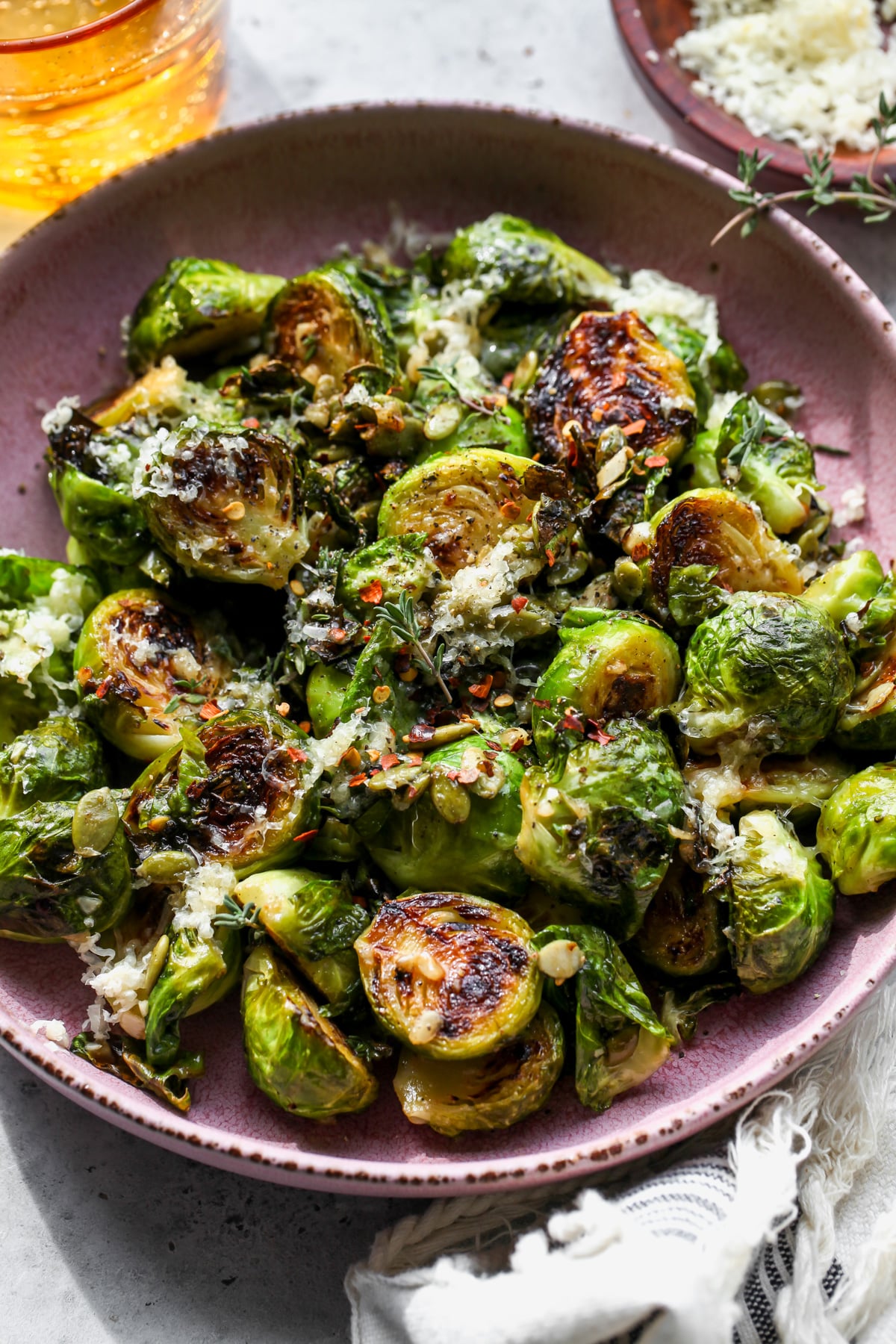 Crispy Brussels Sprouts styled in a wide pink bowl topped with sharp cheddar and pumpkin seeds.
