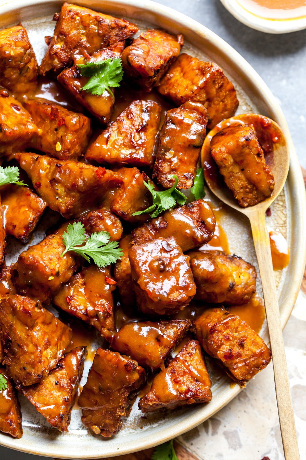 Cubes of marinated peanut baked tempeh styled on a plate with a spoon resting on the right side.