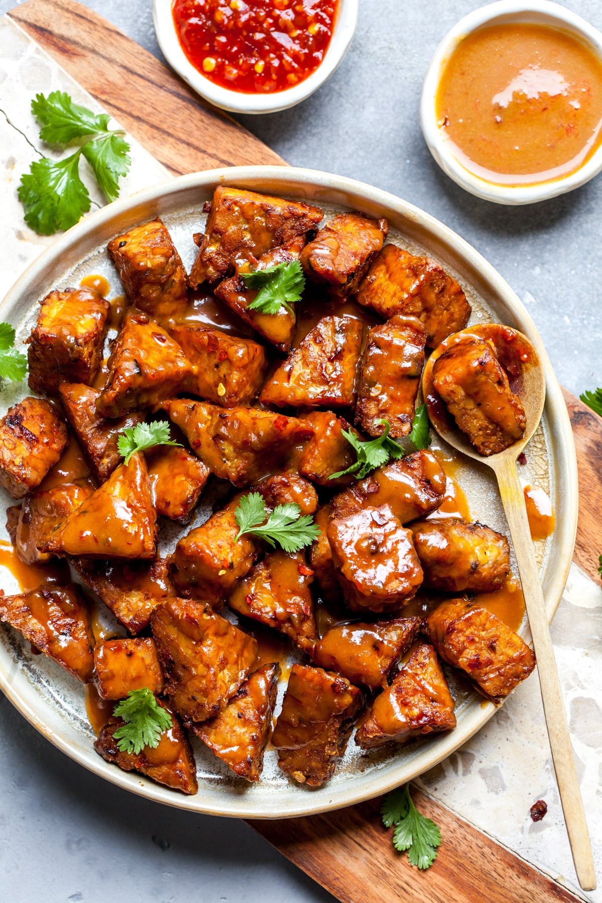 Baked tempeh cut into triangles and coated in peanut sauce styled on a white plate.