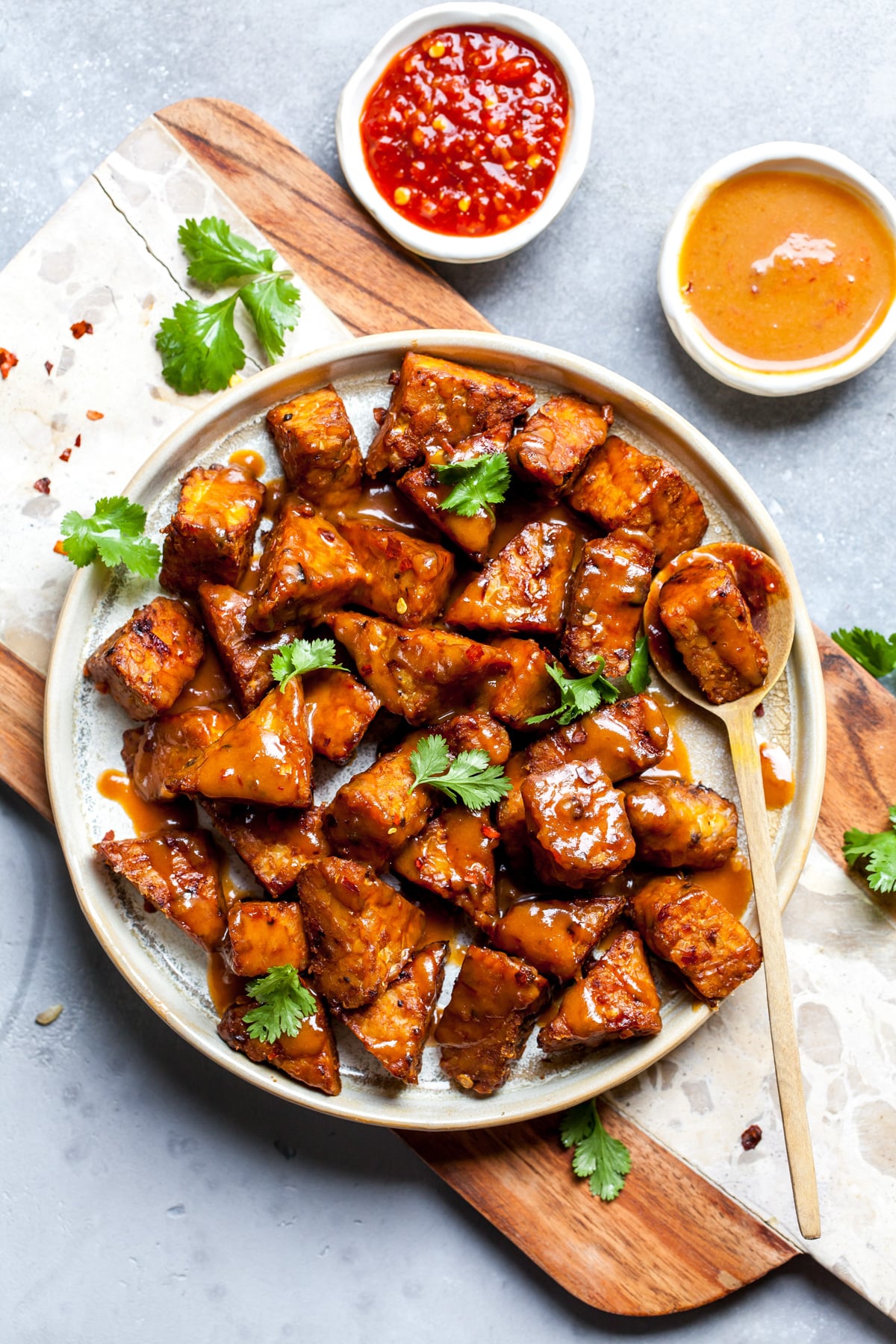 A plate of marinated peanut baked tempeh on a plate with sprigs of cilantro scattered overtop.